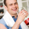 Smiling man with a towel around his neck drinking from a water bottle
