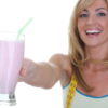 Woman in workout clothes holding a milkshake beside a plate of doughnuts