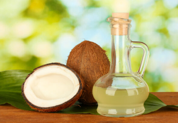 decanter with coconut oil and coconuts on green background